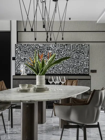 A closer look at the dining setup in the Cuffe Parade apartment. The elegant oval marble table is surrounded by comfortable grey leather chairs, all under a striking modern pendant light fixture, creating a chic and cheerful cocoon.