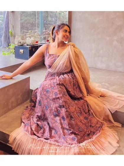 A beautiful mauve printed gown with a pleated texture and a shimmering organza drape. This outfit is the epitome of modern elegance for a cocktail or reception.