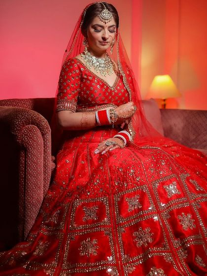 A full-length shot of a bride seated on a couch, her magnificent red lehenga spread out before her.
