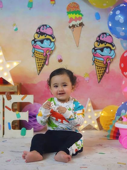 All smiles for his first birthday! This little boy looks so happy in our ice cream themed setup, complete with colourful balloons, a toy ice cream cart, and a big "ONE" sign.