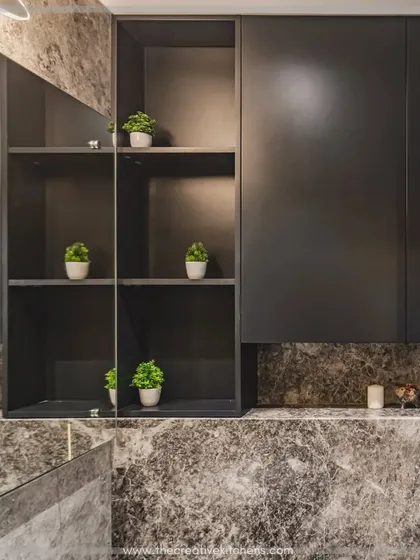 The overhead storage unit combines closed cabinets with open, lit shelving, perfect for displaying decorative items. The large mirror enhances the sense of space and reflects the rich textures of the marble.