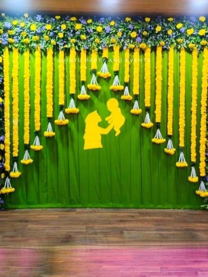 A traditional Seemantham backdrop made of green fabric and marigold flower garlands. A cutout of a mother and child adds a sentimental touch.