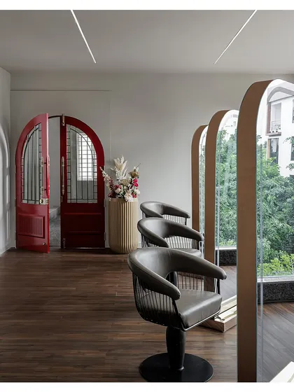 The styling stations are framed by large, arched mirrors that reflect the natural light from the windows. The reclaimed red arched door adds a vintage, eclectic touch against the modern, clean lines of the main space.