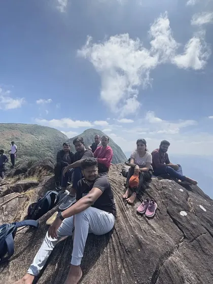 Trekkers resting on a large rock, enjoying the panoramic view from the Kumara Parvatha trail.