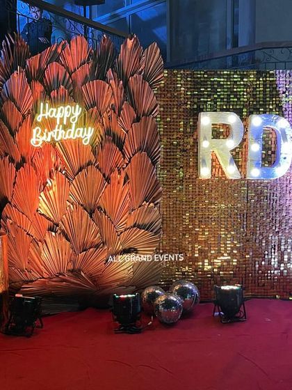 For this outdoor birthday, I used a bold gold shimmer wall and marquee initials. The backdrop is framed with dramatic orange palm leaves and a neon sign, set up on a red carpet for a VIP feel.
