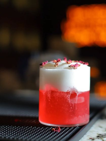 A beautiful layered cocktail with rose-petal garnish. The thick foam and deep red color create a stunning visual.
