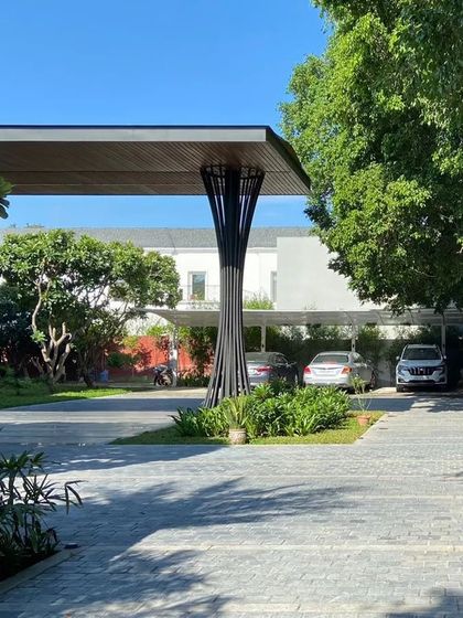The entrance canopy of a modern farmhouse, supported by a sculptural column. This architectural feature, surrounded by greenery, creates a striking and artistic welcome point.