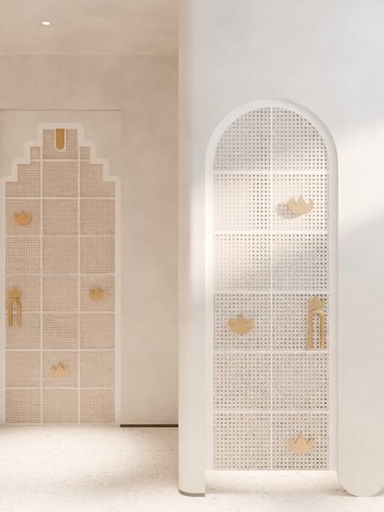 The adjoining washroom continues the dialogue of serenity. Here, arched doorways with cane and lotus-motif details create a sense of purity and awakening, complemented by brass sinks and gold accents.