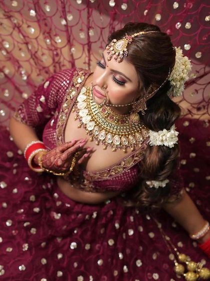 An aerial shot showcasing the intricate details of the bridal lehenga and jewelry. The makeup is designed to be striking from every angle, with highlighted collarbones and a flawless complexion.