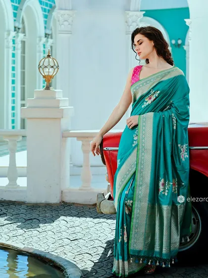 A model for Elezara leaning against a vintage red car. The contrast between the vibrant teal saree and the car creates a visually interesting and stylish campaign image.