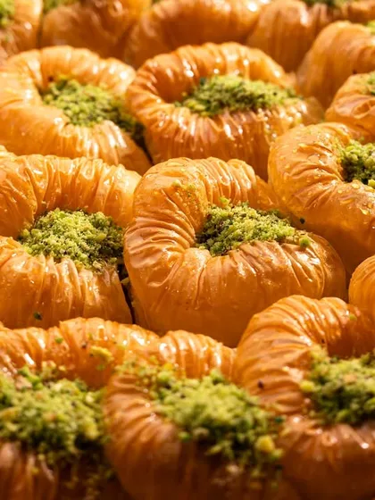 A detailed macro shot of Bülbül Yuvası baklava. The lighting is crafted to emphasize the thousands of flaky filo layers and the vibrant pistachio dust.