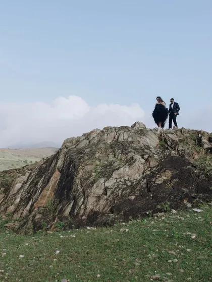 A dramatic wide shot of the couple standing atop a rocky mountain peak, showcasing a sense of adventure and their love story on a grand scale.