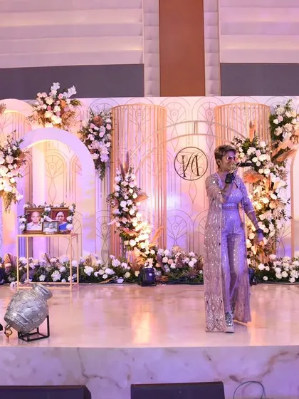 A beautiful stage for a live music performance at a reception, featuring a backdrop of modern arches, soft lighting, and delicate floral arrangements.