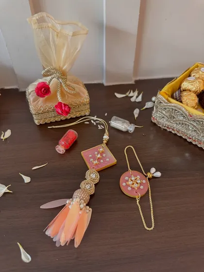 An elegant lumba and rakhi set in shades of peach and pink. The lumba features delicate feather tassels, making it a fashionable and beautiful accessory for your bhabhi.