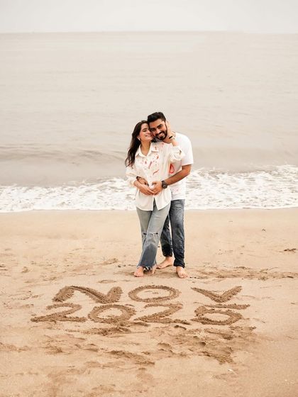 The couple embracing on the beach with "Coming Soon" written in the sand, a simple and classic announcement idea.