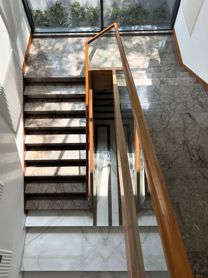 An overhead view of the staircase at Gulmohar Farmhouse, showing the beautiful contrast between the dark marble steps, white marble landing, and warm wood railing.
