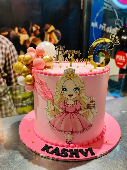 A pretty pink princess cake for Kashvi's 6th birthday. This design features a lovely princess illustration, a gold crown topper, and a cascade of pink and gold decorative balls.