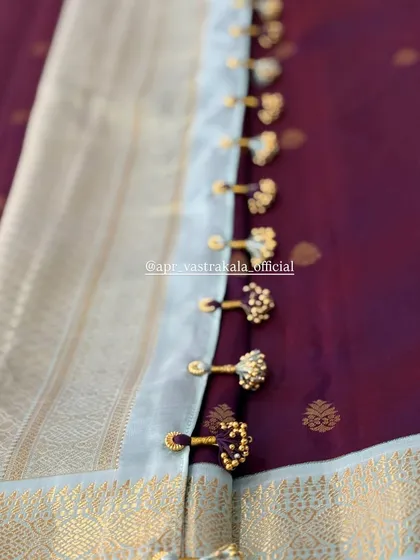 Elegant tassels made of gold beads, adding a subtle, shimmering detail to the border of this deep wine-colored saree.