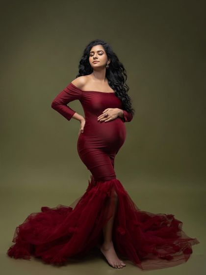 The full silhouette of the red mermaid gown against an olive background. The pose with the leg peeking through the slit adds a touch of modern glamour.