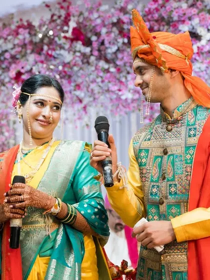 The couple sharing a look during their Sangeet ceremony, microphones in hand, against a backdrop of beautiful cherry blossoms.