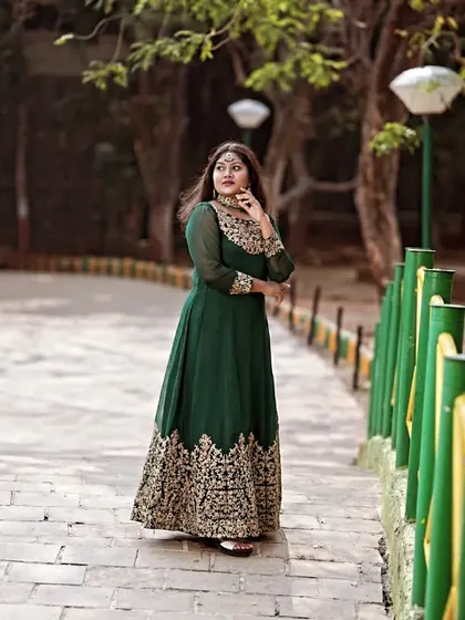 A full-length shot in a park, capturing the elegance of the green Anarkali as the model looks away thoughtfully.