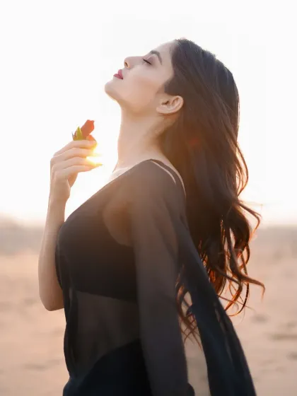 A sensual and serene portrait of a model in a sheer black outfit against the setting sun. The backlighting and the prop rose add a touch of romance and mystery.