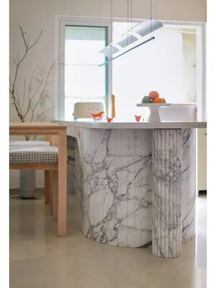 The kitchen's breakfast counter is a true pièce de résistance. Clad in veined marble with a fluted column support, it exudes luxury and serves as a stunning visual anchor for the open-plan space.