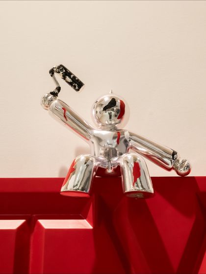 A close-up of the chrome figure atop the "Live Your Best Life" installation, holding a paint roller as if creating the art itself.