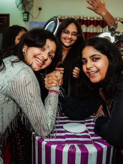 Friends sharing a moment of fun and friendly competition with an arm-wrestling match at a Taylor Swift themed party.