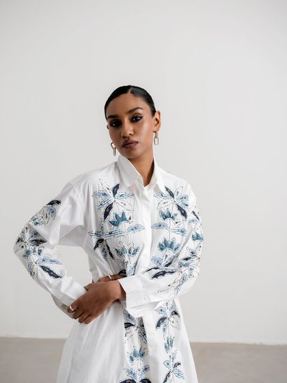 Styling and production for Nakateki, featuring a white shirt dress with blue floral embroidery. The model's pose is strong and confident, reflecting the modern aesthetic of the brand.