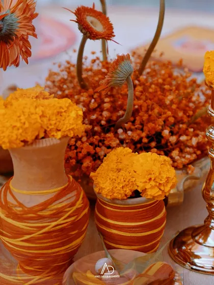 A close-up of the table decor for a traditional event, featuring marigolds and gerberas in rustic, thread-wrapped terracotta pots.