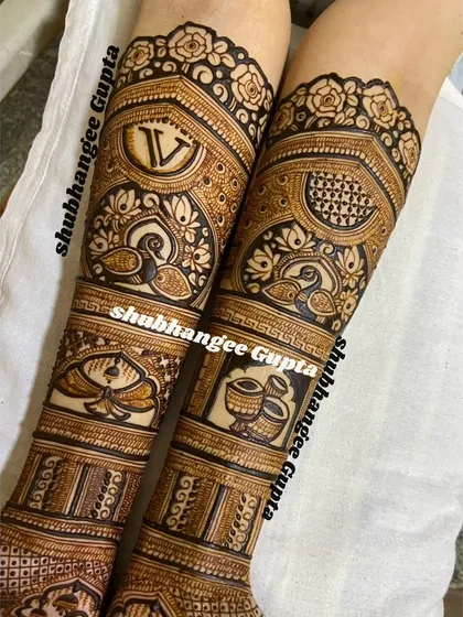 This bridal design tells a story through different panels on the arms. It includes personalized initials, graceful swans, and traditional dholki and shehnai instruments, all woven into an intricate pattern.