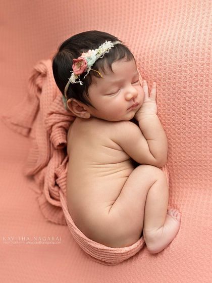A newborn girl in a side-lying pose, wearing a delicate floral headband. This pose is perfect for capturing their tiny profile and curled-up posture in the first 6-14 days.