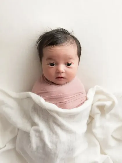 A minimalist portrait of a newborn wrapped in a dusty rose swaddle against a clean white backdrop. This simple composition highlights the baby's alert expression and delicate features.