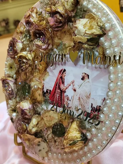 This oval resin frame is a beautiful example of how I can preserve your wedding varmala. I arranged the dried roses and other flowers around the couple's photo and added a border of pearls to create a classic, elegant look. It’s a wonderful centerpiece for a side table.