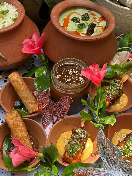 An Asian-themed platter featuring crispy spring rolls and savory skewers, served in rustic earthenware with beautiful floral and butterfly decorations.