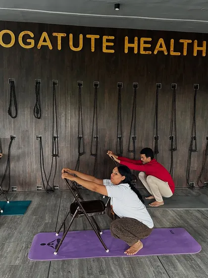 This is a supported Malasana (Garland Pose) using a chair. It allows the student to work on hip opening and spinal lengthening while the chair provides stability and reduces strain on the knees and ankles.