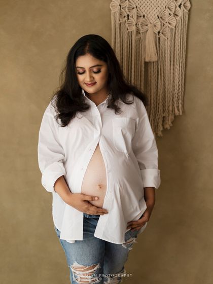 A quiet moment of reflection, looking down at her bump with love. The simple white shirt and jeans keep the feeling honest and real.
