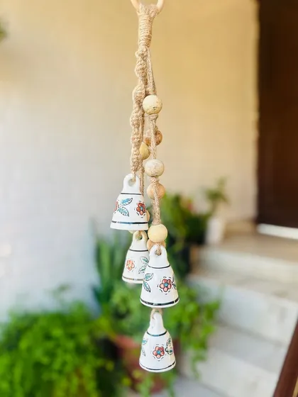 A close-up of our 'Symphony Chimes' in the 'Rustic' variant, hanging outdoors. The combination of hand-painted ceramic bells, wooden beads, and jute macrame knots creates a beautiful, natural look.