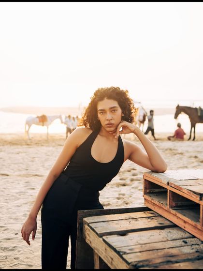 A relaxed pose using a wooden pallet as a prop. The background shows the life of the beach, adding an authentic, candid feel to this fashion shot.