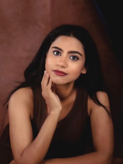 A simple and classic studio headshot against a warm, textured brown background. Her expression is calm and direct, creating a timeless portrait.