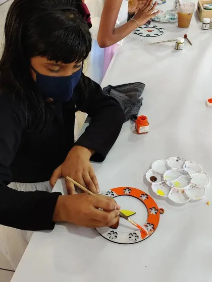A child carefully paints an orange and white design on a wooden hanging for Diwali. We provide all the materials for these festive crafts.