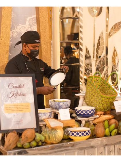 A chef at our "Coastal Kitchen" live station, which is decorated with regional elements like coconuts and woven baskets. We create themed stations that transport guests to different culinary regions through both food and presentation.