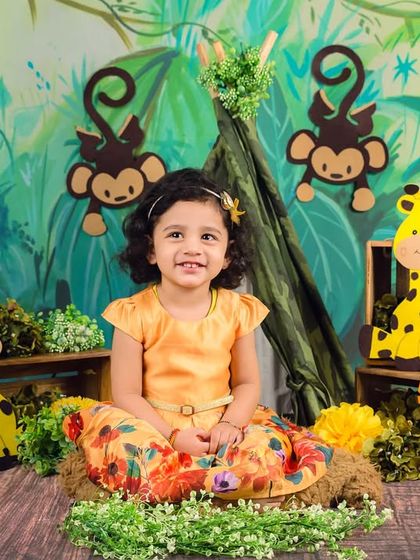 A slightly older toddler smiles sweetly in her jungle-themed setup, looking poised and happy.