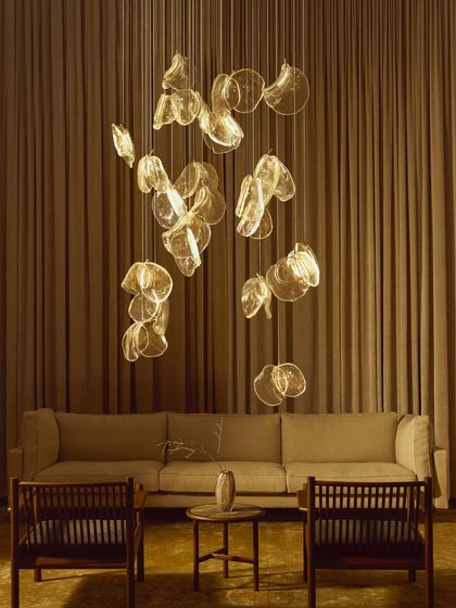 A large installation of the Bocci 141 series hangs above a living room seating area, creating a warm, golden canopy of light.