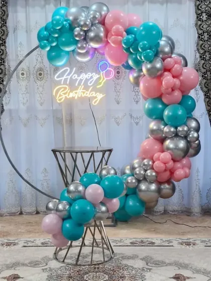 A trendy color combination of teal, pink, and silver chrome balloons on a circular frame with a neon sign.