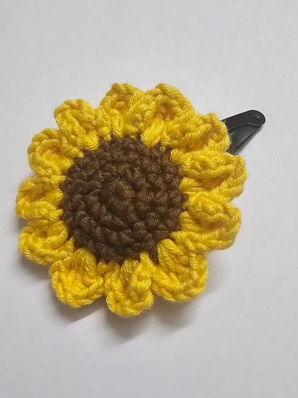 A close-up product shot of my handmade crochet sunflower hair clip. I use a blend of acrylic and cotton yarn to create the detailed petals and center.