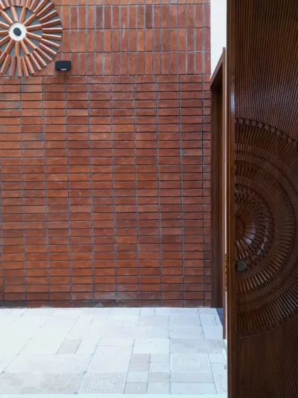 Craftsmanship is at the core of my work. This entrance features a custom-carved wooden door that echoes the circular motifs on the terracotta brick wall. It's a beautiful example of how we let the materials and the skill of the artisans tell the story, creating a welcome that is both personal and unforgettable.