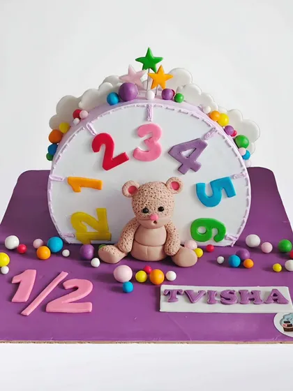 A "cake top forward" design for a half birthday celebration. This unique style shows a clock face with a teddy bear, marking the 6-month milestone in a creative way.