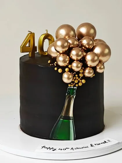 A chic and modern 40th birthday cake with a champagne bottle theme. The design features a cascade of golden chocolate spheres bubbling out of an edible bottle image on a sleek black cake.